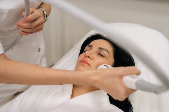 Close-up of relaxed woman with closed eyes receiving microneedle radiofrequency face lifting procedure from dermatologist for skin tightening and rejuvenation in professional aesthetic clinic.
