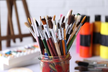 Fototapeta premium Paintbrushes in holder and paints on light table, closeup