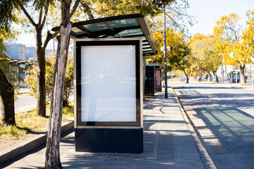 Vertical blank billboard at a bus stop shelter in Buenos Aires, Argentina, during autumn season. Mockup lightbox with copy space for advertising or poster display in a city setting. © Nina Abrevaya