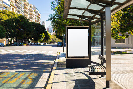 Vertical blank billboard at a bus stop shelter in Buenos Aires city, Argentina. Mockup lightbox with copy space for advertising or poster display in a city setting.