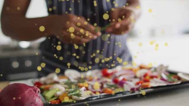 Cook reaching for herbs tearing arranging veg on tray for food roasting, gold bokeh covering hands