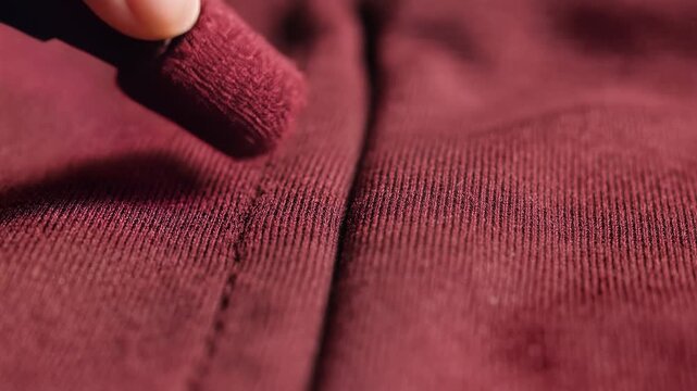 Closeup of a hand using an eraser on a burgundy fabric seam.