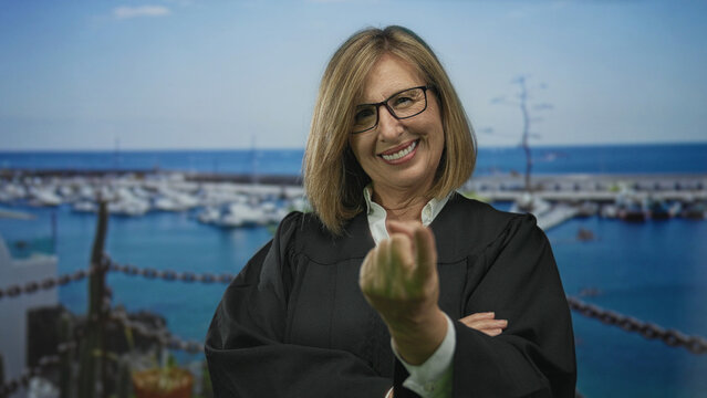 Woman in black judge robe wearing glasses beckons hand in building overlooking a marina and boats by the sea; confidence.