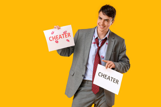 Happy man with kiss marks on his shirt holding paper sheets with word CHEATER against yellow background