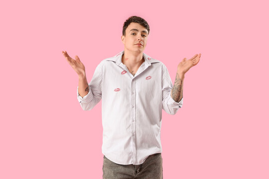 Embarrassed man with kiss marks on his shirt against pink background