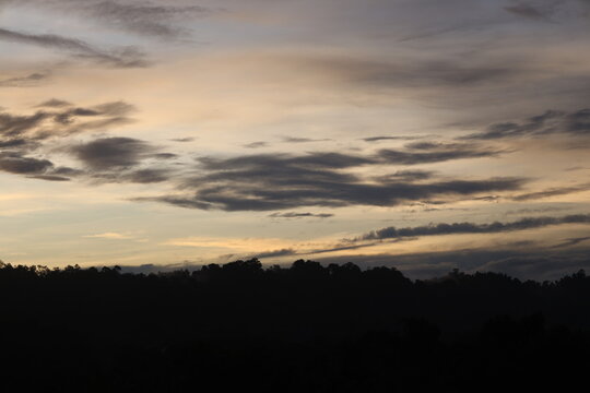 low dark clouds scudding above ridge line in shadow as distant first light beckons (wide-angle, panorama, sunrise, tropical)