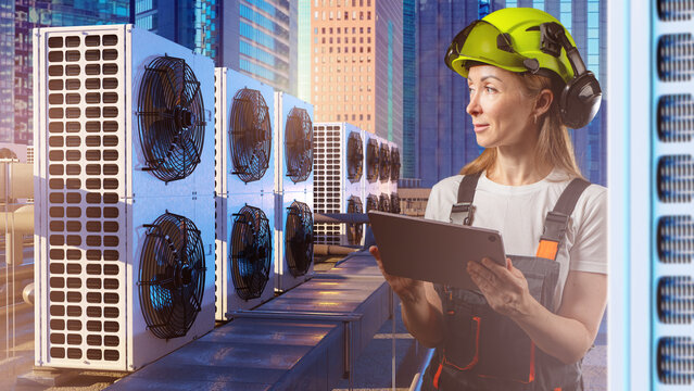 HVAC service, Technical inspection. Female technician checks rooftop air conditioning units on tablet during equipment monitoring in urban commercial area.