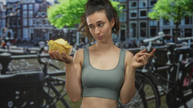 Woman pointing at a clear bowl of potato chips by a canal with a dubious look on her face; indecision choice.