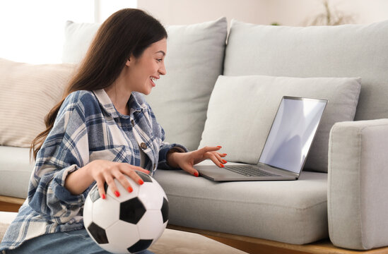 Happy young woman with soccer ball using laptop at home. Sports bet concept