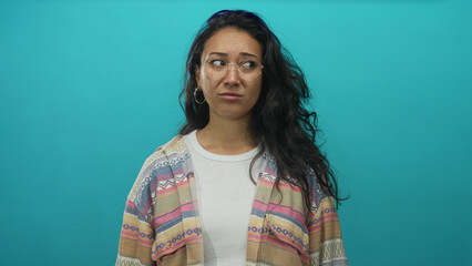 Woman with glasses touching forehead in studio teal backdrop with hand near mouth and hoop earring visible  concern. © Krakenimages.com