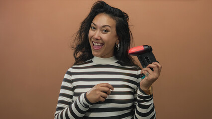 Woman holding video game controller and smiling in peach studio, striped top visible, showing tattooed hand and hoop earring  playful joy. © Krakenimages.com