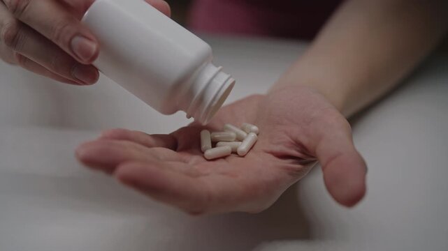 Person taking white capsule pill from bottle for medical treatment, concept importance of medication and daily dosage for maintaining health and wellness, close-up, slow motion.
