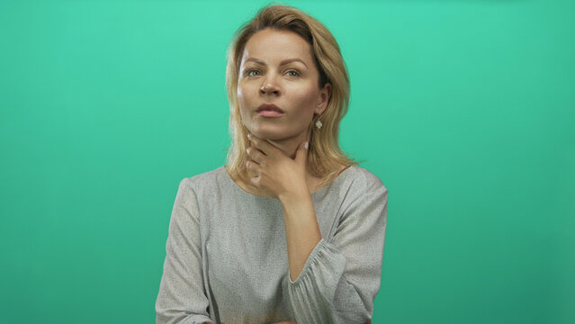 Woman touches chin in green studio while tilting head upward with thinking gesture and steady gaze; curiosity.