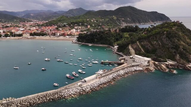 Aerial view of the Sestri Levante promontory featuring the historic harbor, colorful rooftops, and lush green hills under a cloudy sky in Sestri Levante, Liguria, Italy.