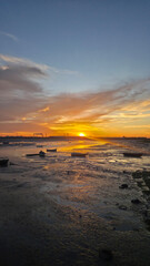 Fototapeta premium Vibrant sunset sky with dramatic clouds reflected on calm coastal water with small boats. Rich colors and contrast create a striking evening landscape.