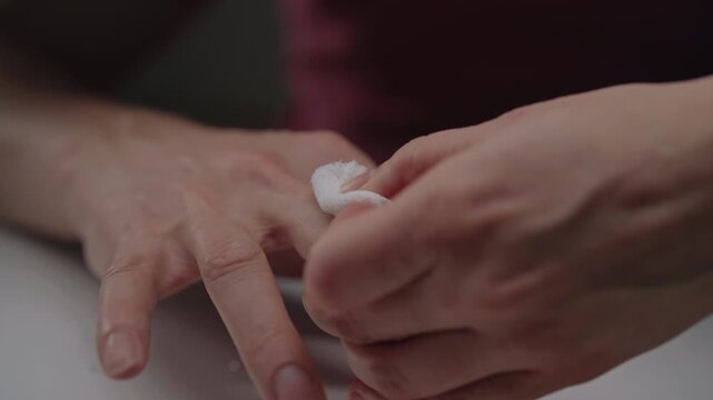 Man treating bleeding cut on finger with cotton, providing first aid for minor injury and stopping bleeding from the fresh wound after accident, close-up. Shooting in slow motion.