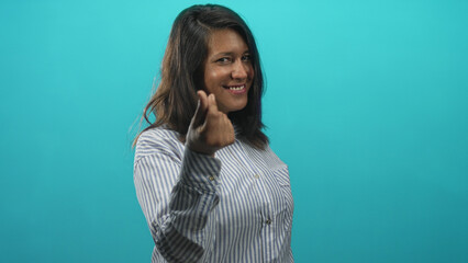 Fototapeta premium Woman smiling and making finger heart with hands wearing striped shirt in studio with turquoise backdrop; friendly affection warmth connection.