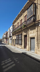 Fototapeta premium Narrow street with traditional historic buildings, balconies with flowers and bright sunlight. Authentic European architecture and calm urban atmosphere.