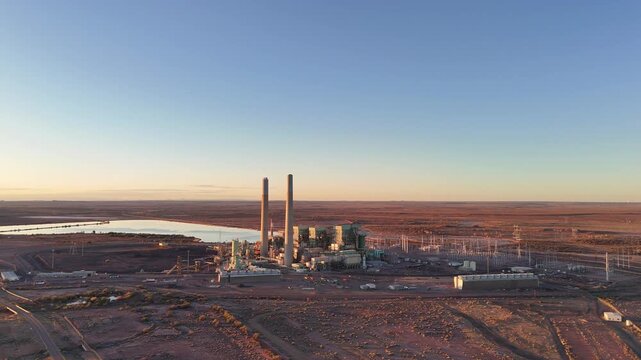Aerial view of Cholla Power Plant with tall smokestacks and cooling pond in the desert landscape at sunset Joseph City, Arizona, United States.