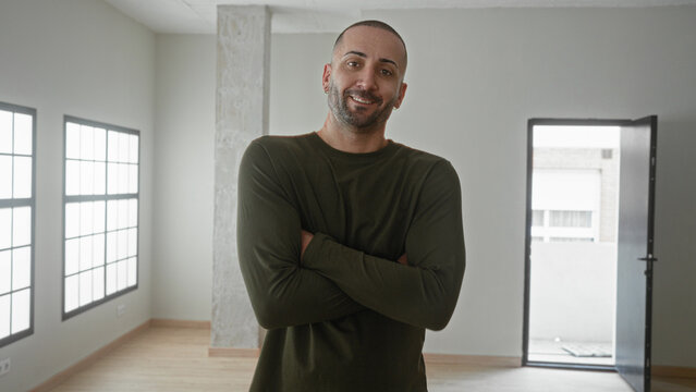 Man arms crossed in empty building room with open door, large windows and concrete pillar; confident new home.