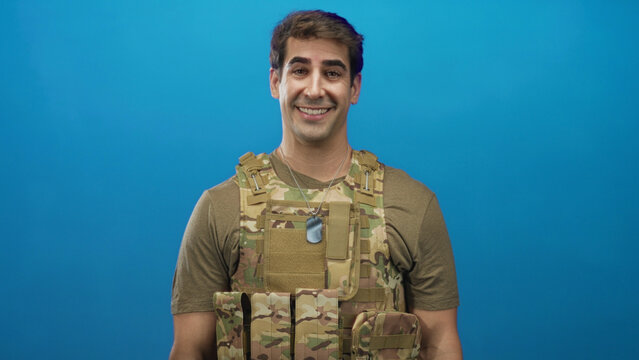 Man soldier in multicam tactical vest with dog tags looks down and occasionally smiles in studio; reflective duty.