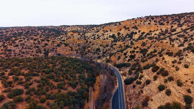 Winding asphalt road through green and red hills in Spain. High angle view of a curved road between shrubland and red clay slopes in Aragon region.