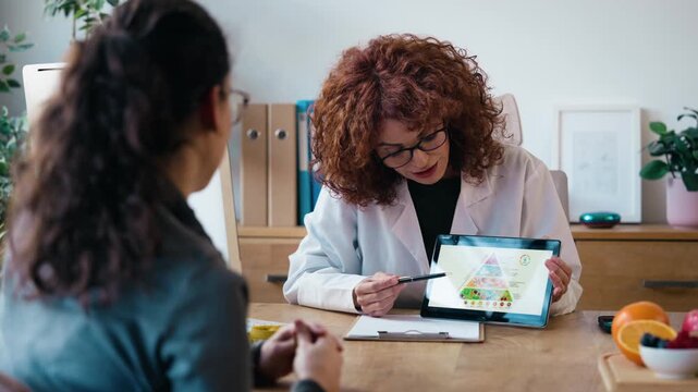 Video of nutritionist woman explaining the food pyramid to a patient using a digital tablet in a hospital consultation