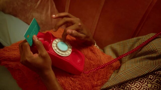 Close up of man dialing an old vintage rotary phone while holding a credit card, person making a payment or phone order using retro telephone and plastic card in high quality cinematic 4k.