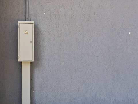 Exterior Electrical Junction Box with Hazard Symbol on Grey Wall &mdash; Urban Infrastructure Electricity Safety Concept with Copy Space