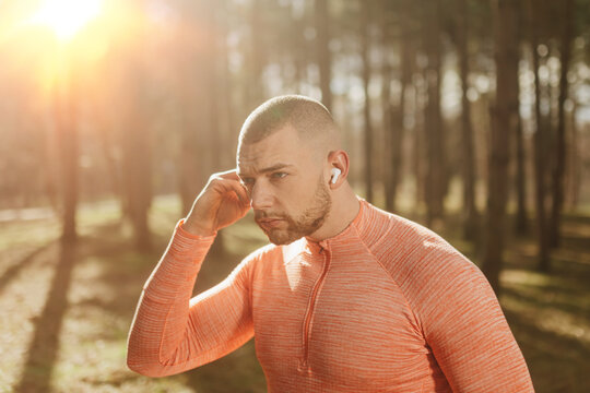 Man runs outside in the forest while listening to music during sunset with wireless earbuds on a cool day