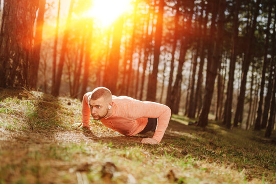 Man doing push-ups in the forest during sunset while listening to music