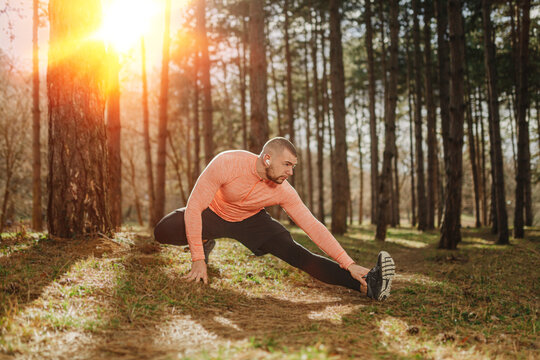 Man stretches in a forest during sunset while preparing for exercise and enjoying the fresh air
