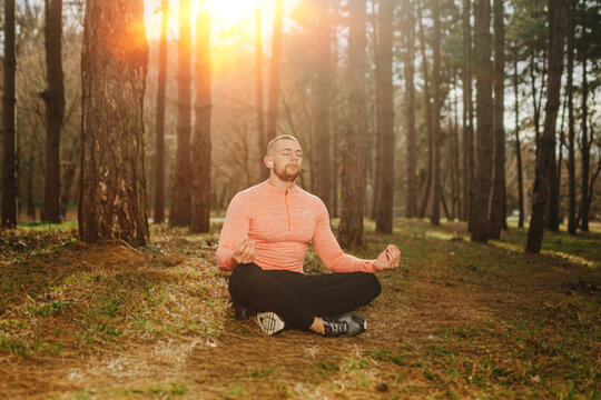Man practices meditation in a forest during sunset while sitting on the ground and connecting with nature