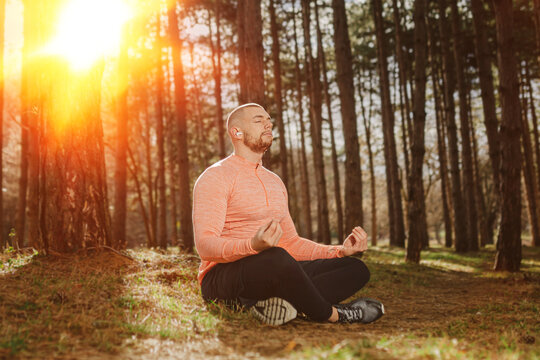 Man sits in a forest and practices meditation while sunlight shines in the background during the day
