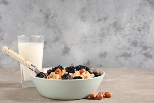 Bowl of tasty oatmeal with prunes, hazelnuts and glass of milk on table