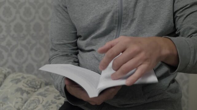 Reading quietly indoors. Person flipping pages in cozy space. Closeup of hands and spine during calm reading session. An intimate moment of reading with deliberate page turns in homely environment
