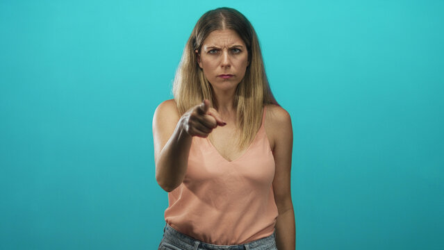 Woman pointing finger, bare shoulder visible, stern expression in studio with turquoise backdrop; accusation anger.