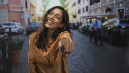 Obraz premium Woman pointing finger toward camera on a busy city street with parked cars and blurred pedestrians; playful invitation.