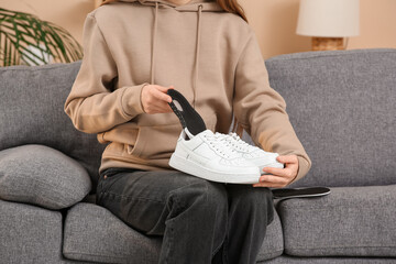 Young woman putting orthopedic insole into sneaker on sofa at home