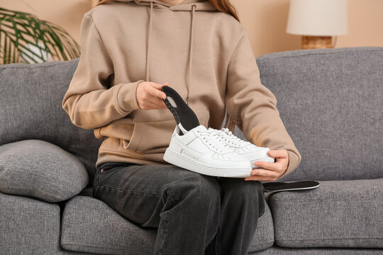 Young woman putting orthopedic insole into sneaker on sofa at home