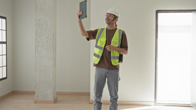 Man architect holds tablet aloft with one hand and hand on hip in building; site inspection confidence.