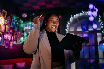 Smiling woman creating digital content on tablet in night club environment with colorful neon lights creative professional lifestyle authentic representation inclusion and success smiling © BullRun