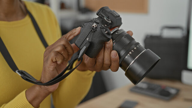 Woman adjusts camera with hands and taps dials on lens while holding strap in studio; concentration craft practice.