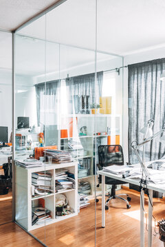 Modern glass-walled office with desks and paper clutter