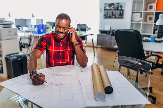 Smiling architect on phone sketching plans in studio