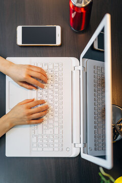 Hands typing on laptop at modern desk with phone and drink