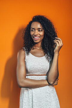Smiling woman in white dress posing against orange wall