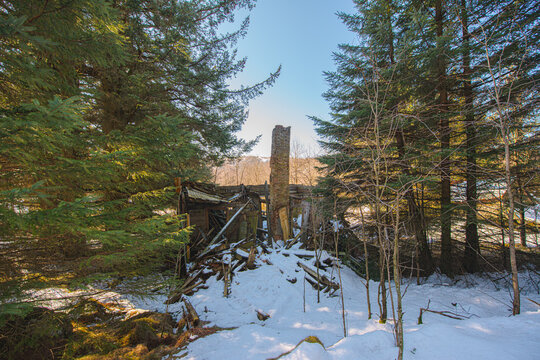 Ruined abandoned cabin chimney standing in snowy forest landscape.