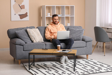 Fototapeta premium Handsome man using laptop on sofa in living room