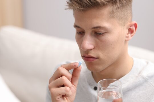Depressed man with glass of water taking antidepressant indoors, space for text